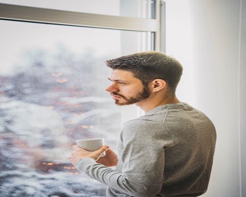 Person standing near a window looking out thoughtfully
